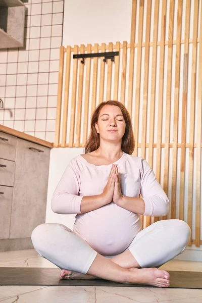 임신 한 젊은 여성 이 주방에서 요가를 연습하고 있습니다. 온라인 건강 관리 강좌 — 스톡 사진