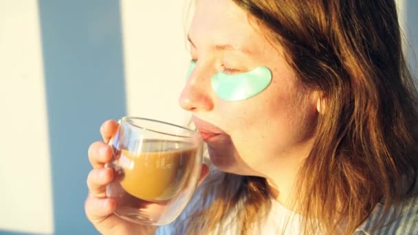 Una joven bebe café en casa. Rutina. Parche ocular para la salud de la piel — Vídeos de Stock
