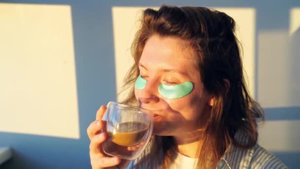 Młoda kobieta pije kawę w domu. Dzień dobry. Przepaska na oczy dla zdrowia skóry — Wideo stockowe