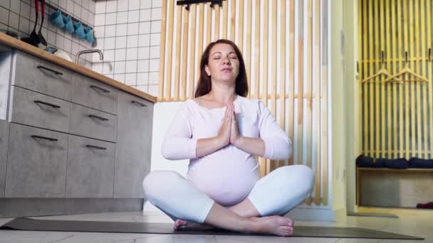 Mujer embarazada joven haciendo ejercicio de yoga en la cocina. Cuidado de la salud lecciones en línea — Vídeo de stock