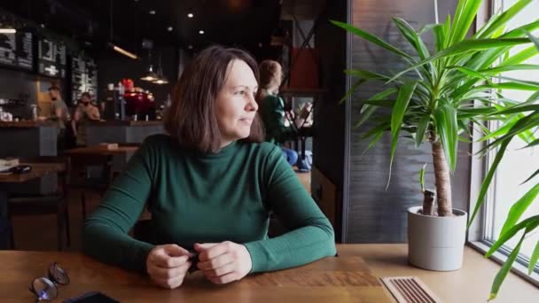 Bonita mujer sentada en la cafetería y hablando. Vestido verde con mangas largas — Vídeos de Stock