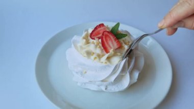 Çay kaşığı Pavlova tatlısını kırar. Masada beyaz kremalı tatlı yemek