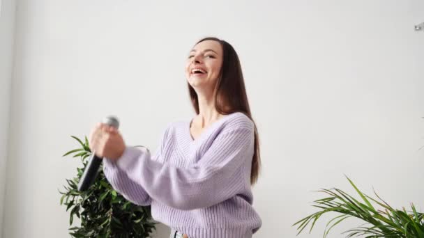 Een jonge vrouw zingt thuis. Karaoke zwarte microfoon. Huisliedjes dansen. — Stockvideo