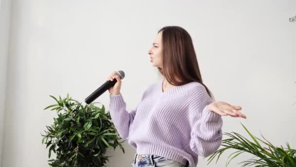 Genç kadın evde şarkı söylüyor. Karaoke siyah mikrofon. Şarkı sözleri dans ediyor. — Stok video
