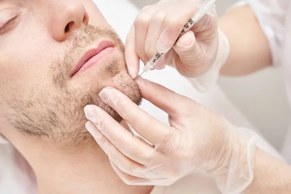 Spritze im Wellness-Salon. Der Arzt legt Handschuhe an. Nahaufnahme. Hübscher männlicher Patient Stockfoto