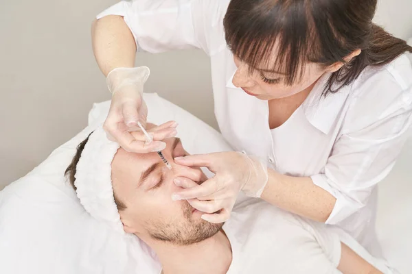 Spritze im Wellness-Salon. Der Arzt legt Handschuhe an. Nahaufnahme. Hübscher männlicher Patient — Stockfoto