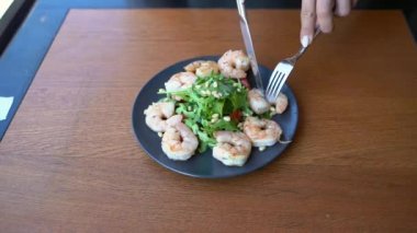 Restoranda karides salatası yiyen genç bir kadın. Sağlıklı gıda konsepti. Çatal, bıçak.