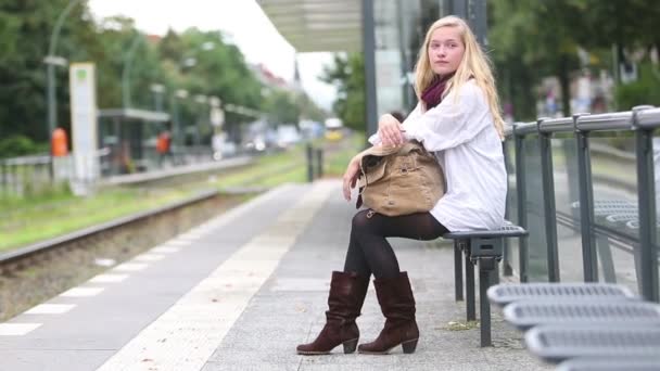 Sitzende junge Frau wartet auf öffentliche Verkehrsmittel — Stockvideo