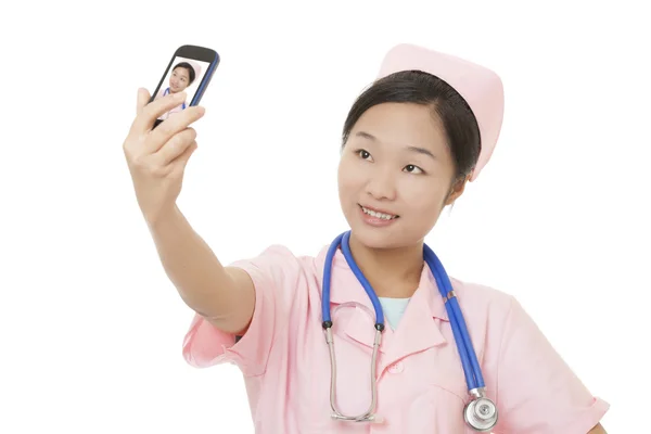 Linda enfermeira asiática usando uma foto celular para tirar uma selfie de si mesma isolada em um fundo branco — Fotografia de Stock