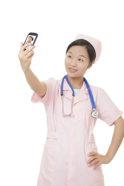 Linda enfermeira asiática usando uma foto celular para tirar uma selfie de si mesma isolada em um fundo branco — Fotografia de Stock