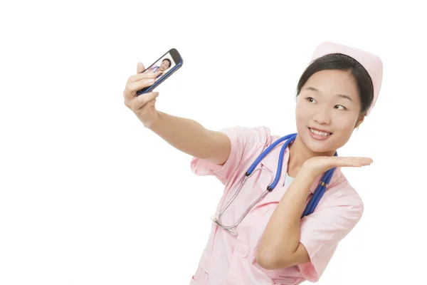 Linda enfermeira asiática usando uma foto celular para tirar uma selfie de si mesma isolada em um fundo branco — Fotografia de Stock