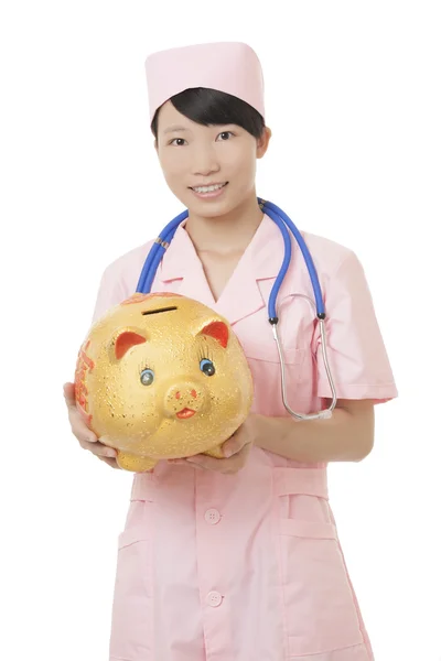 Schöne asiatische Krankenschwester hält ein Sparschwein isoliert auf weißem Hintergrund. Veranschaulichung der hohen Kosten der medizinischen Versorgung — Stockfoto