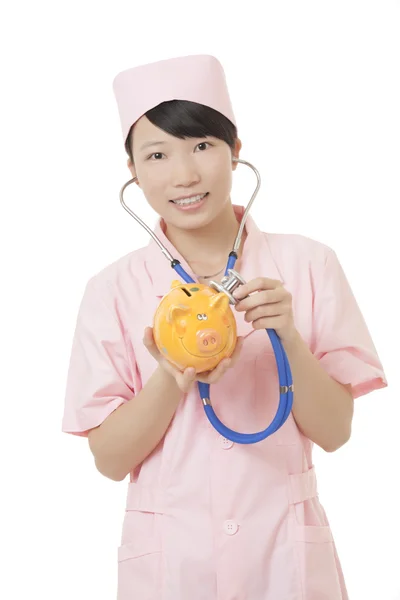 Beautiful Asian nurse holding a piggy bank isolated on a white background.  Illustrating the high cost of medical care — стокове фото