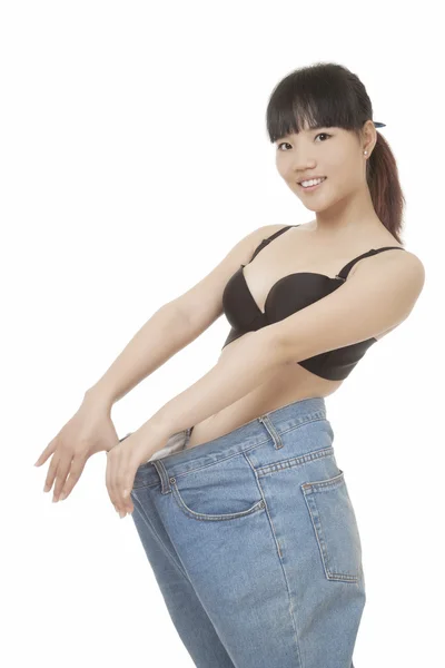 Hermosa mujer china con pantalones vaqueros gordos para ilustrar la pérdida de peso aislada sobre un fondo blanco —  Fotos de Stock