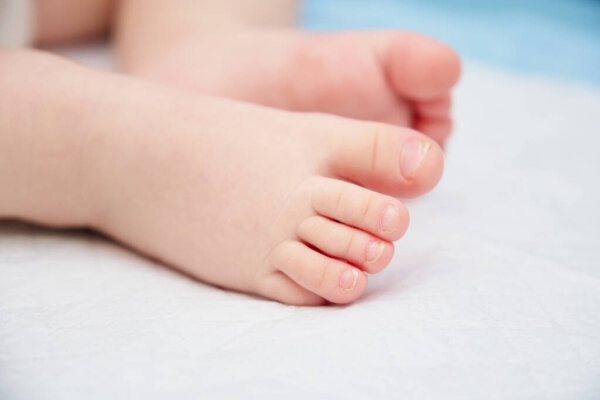 Маленькие ножки новорожденного ребенка на белом одноразовом подгузнике крупным планом