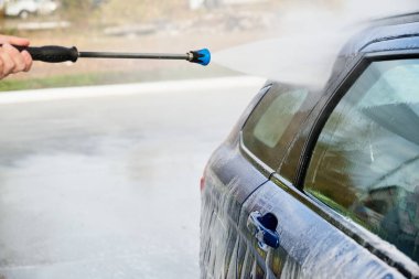 Serviste çalışan bir adam, arabayı köpük ve hortumla yıkıyor.