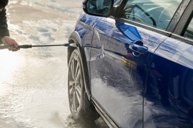 Serviste çalışan bir adam, arabayı köpük ve hortumla yıkıyor.