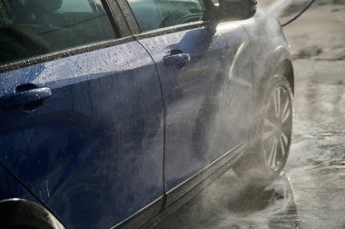 Serviste çalışan bir adam, arabayı köpük ve hortumla yıkıyor.