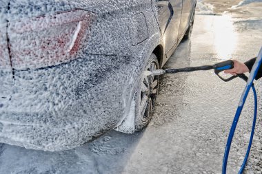 Serviste çalışan bir adam, arabayı köpük ve hortumla yıkıyor.