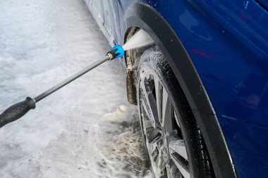 Serviste çalışan bir adam, arabayı köpük ve hortumla yıkıyor.