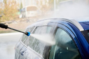 Serviste çalışan bir adam, arabayı köpük ve hortumla yıkıyor.