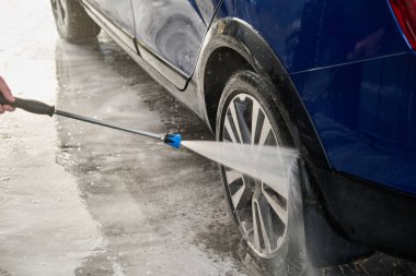 Serviste çalışan bir adam, arabayı köpük ve hortumla yıkıyor.