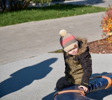 Sıcak giysiler içinde küçük bir çocuk bir bankta oturur ve yüzünü çevirir.