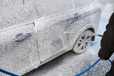Serviste çalışan bir adam, arabayı köpük ve hortumla yıkıyor.