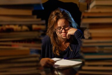 Gözlüklü güzel bir kadın final sınavları için kütüphanede ders çalışıyor..