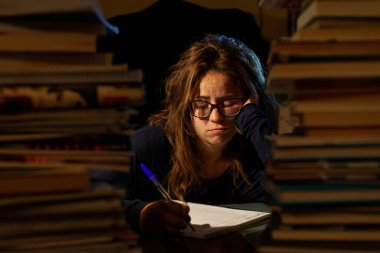 A beautiful woman with glasses studying in a library for her final exams. clipart