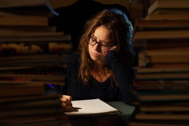 Gözlüklü güzel bir kadın final sınavları için kütüphanede ders çalışıyor..