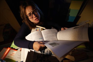 Gözlüklü güzel bir kadın final sınavları için kütüphanede ders çalışıyor..