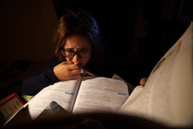 Gözlüklü güzel bir kadın final sınavları için kütüphanede ders çalışıyor..