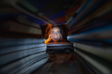 Sınavlar için kütüphanede okuyan aşırı yüklenmiş bir kadın.