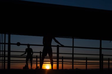Gün batımında Portekiz 'de bir sahil yolunda futbol oynayan iki gencin silüeti.