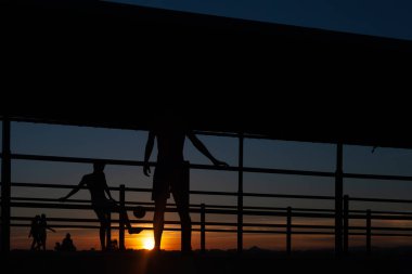 Gün batımında Portekiz 'de bir sahil yolunda futbol oynayan iki gencin silüeti.