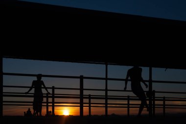 Gün batımında Portekiz 'de bir sahil yolunda futbol oynayan iki gencin silüeti.