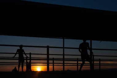 Gün batımında Portekiz 'de bir sahil yolunda futbol oynayan iki gencin silüeti.
