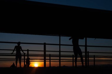 Gün batımında Portekiz 'de bir sahil yolunda futbol oynayan iki gencin silüeti.