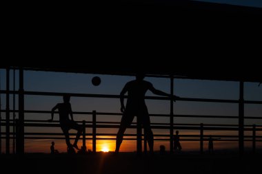 Gün batımında Portekiz 'de bir sahil yolunda futbol oynayan iki gencin silüeti.
