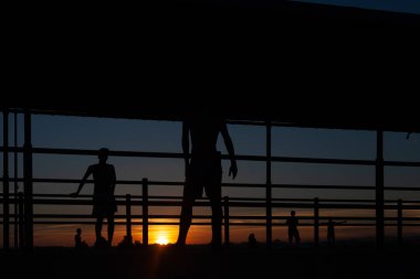 Gün batımında Portekiz 'de bir sahil yolunda futbol oynayan iki gencin silüeti.