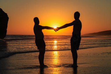 Bir eşcinsel çift gün batımında sahilde poz verir.