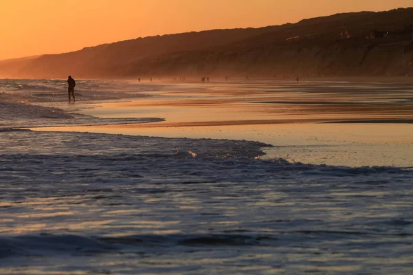 Okyanusun üzerinde yürüyen bir adamın silüetiyle uzun bir gün batımı görüntüsü.
