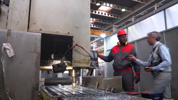 アフリカ系アメリカ人と話す品質管理インスペクター工場でCncフライス盤オペレータ Cnc工作機械切削鋼 Cncコントローラの隣で話す多人種間産業労働者 — ストック動画
