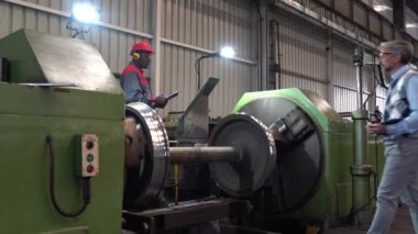 Torna makinesinin yanındaki Kafkas Kalite Kontrol Müfettişi ile konuşan Afro-Amerikan CNC makine operatörü Çelik Tren Tekerlek Üretimi. Yapım Müdürü Siyah İşçiye Emir Veriyor.