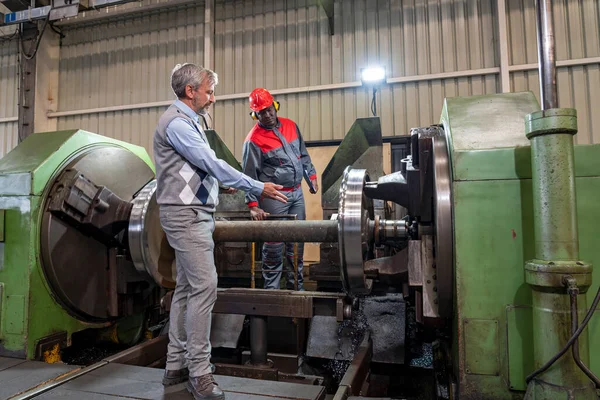 多人種労働者が機械の横に立ち 話しています 車輪の製造を訓練する 鉄道工場でアフリカ系アメリカ人Cnc機械オペレーターに注文を与える生産マネージャー — ストック写真