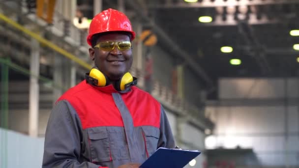 穿着防护服的年轻的非洲裔美国工人拿着剪贴板微笑 并在镜头中抛出抛出抛物线 护目镜 工作服中的黑人产业工人的肖像 — 图库视频影像