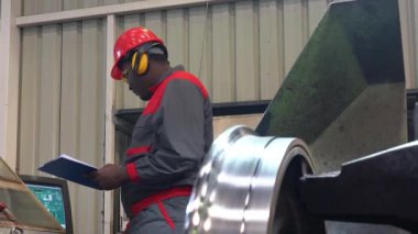 Torna makinesinde demiryolu tekerleği üretim sürecini izleyen Afro-Amerikan CNC makine operatörü. Siyah Endüstri İşçisi CNC Torna Makinesi Kontrolörünün yanında duruyor. 