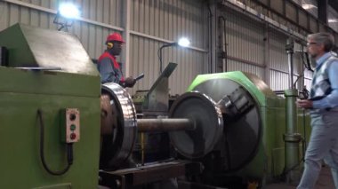 Kafkas Üretim Yöneticisi ile konuşan Afro-Amerikan CNC makine operatörü Torna Makinesinin yanında - Demiryolu Tekerleği Üretimi - Yakınlaştır. Dijital Tablo Kullanılan Üretim Yöneticisi.