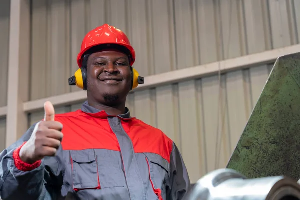 微笑的非裔美国人蓝领工人在一家工厂里抛出枪弹 红盔黑工的肖像 听觉保护器及工作服 — 图库照片